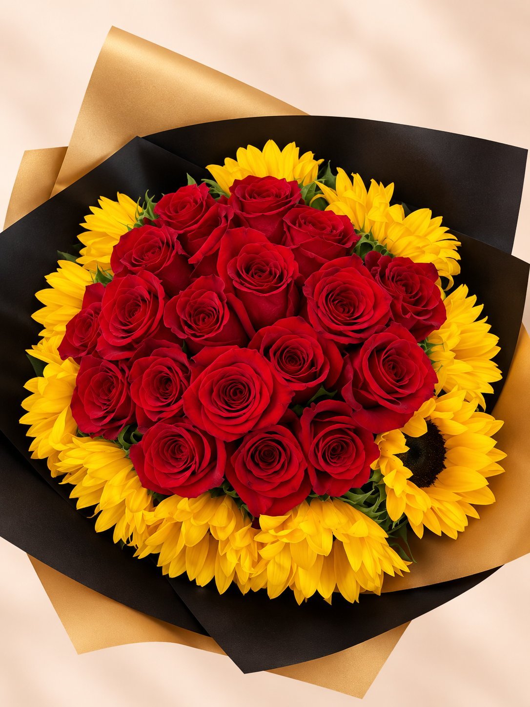Flower bouquet with red roses in center surrounded by yellow sunflowers, wrapped in black and gold paper